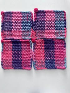 Four mug rugs in color combination of reds, pinks, blues, and purples.
